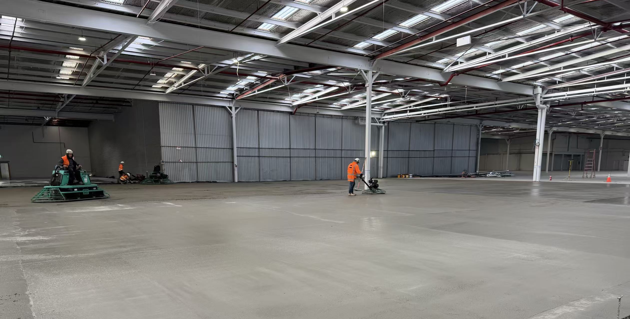 Workers finishing a concrete floor inside an existing industrial factory
